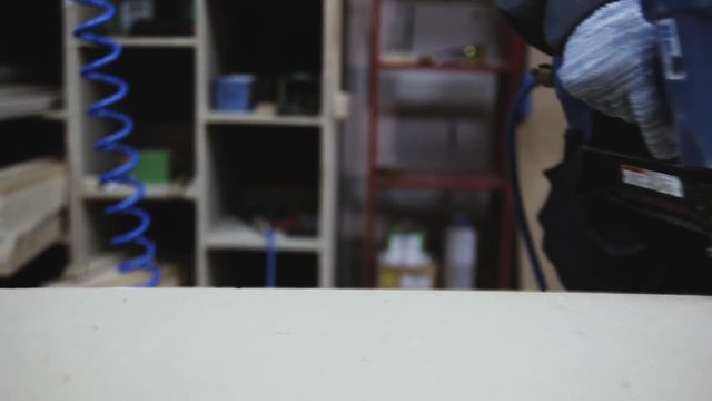 Worker repairing furniture with industrial construction stapler. Close-up of carpenter's hands, which clogs metal staples in wooden board with pneumatic stapler pistol. Industrial stapler for staples.