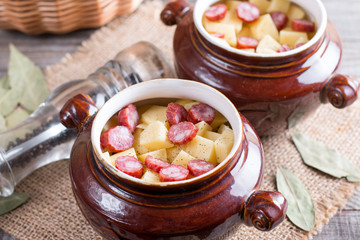 Hot potato goulash with bacon and Vienna sausages served in a ceramic bowl with on an old wooden table
