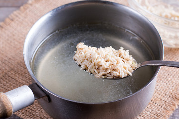 Rice in a spoon in a saucepan with boiling broth on a wooden table