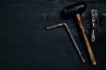 Old, rusty tools lying on a black wooden table. Hammer, chisel, metal scissors, wrench.
