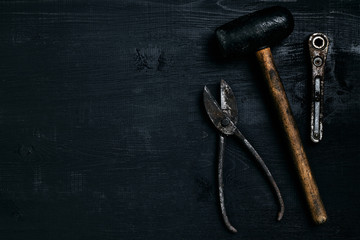 Old, rusty tools lying on a black wooden table. Hammer, chisel, metal scissors, wrench.