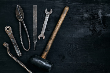 Old, rusty tools lying on a black wooden table. Hammer, chisel, metal scissors, wrench.