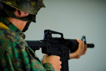 Portrait of young soldier holding in his hands a rifle, wearing a military uniform, in a gray background