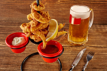 Squid rings in batter with lemon, red and white sauces on wooden table