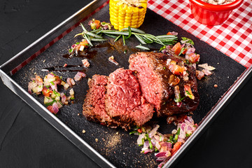 Sliced medium rare grilled Beef steak Ribeye with corn, rosemary, onion and mushroom sauce on a metal tray on a black background