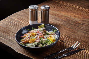 Caesar salad. Caesar dressing is sour taste of vinegar. Often served with Green Cos, topped with Parmesan cheese Costa biscuits, bacon and egg. Dark plate on wooden background