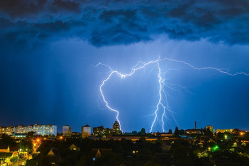 Lightning over the city in the night sky strikes the roof of the house