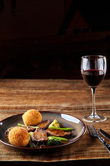 Stewed beef with vegetables and a glass of red dry wine on wooden table, close up. Hot Meat Dishes.