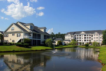 Fototapeta na wymiar Southern modern architecture and vacation rentals background. Myrtle Beach suburb neighborhood morning view with buildings around the pond with sprinkling fountain. South Carolina, USA.
