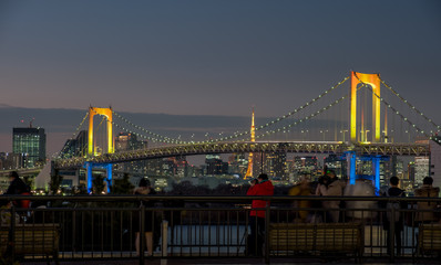 The Iluminated Rainbow Bridge viewed at sunset watched by a crowd of people