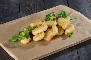 nuggets/ Appetizing slides of nuggets on paper on a wooden table with green parsley sprigs.