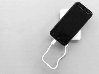 A black smartphone charging with a white powerbank set on gray background. Selective focus with copy space.