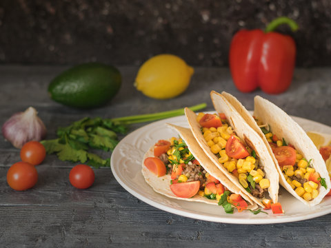 Freshly prepared Mexican tacos on a plate on a dark table with vegetables.
