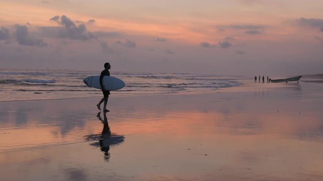 Surfer walks along the beach with his surfboard during sunset. Taken in Nicaragua.