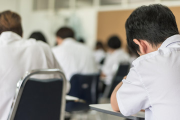Obraz premium Blur education background school or university students writing answer doing exam in classroom, view from back of the class