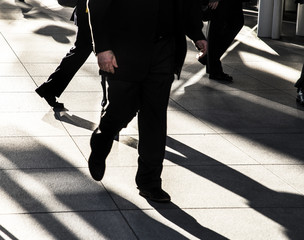 Businessman walking quickly on city sidewalk wearing black suit with crowd of businessmen...