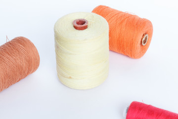 Four reels of colored thread on a white background. The spool of thread yellow, orange, red and...