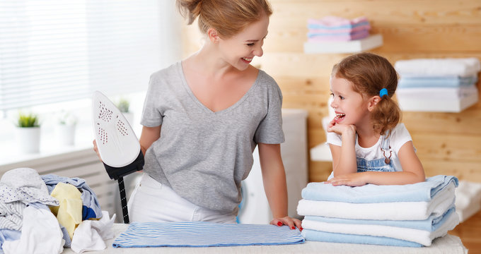 Happy family mother housewife and child daughter ironing clothes   in laundry
