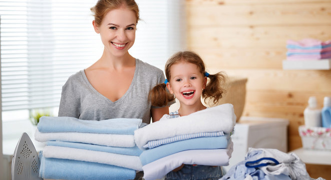 Happy family mother housewife and child daughter ironing clothes   in laundry