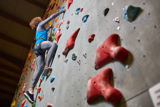 Young sportsman grabbing by grips on climbing wall while moving upwards