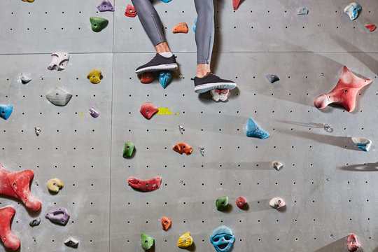 Lower part of climber legs in leggins and sports-shoes standing on grips of wall