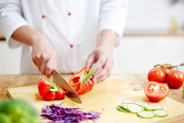 Chef of restaurant cutting red pepper in two halves while cooking meal from vegs