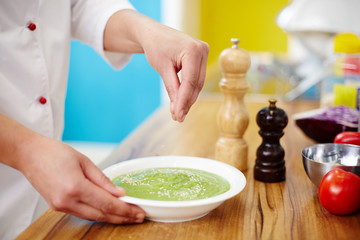 Hands of chef sprinkling fresh vegetable smoothie in plate with sesame seeds