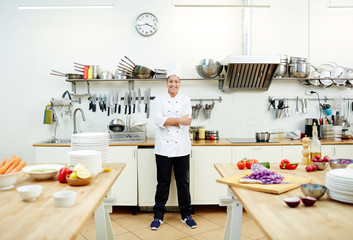 Cheerful professional chef in uniform looking at camera in the kitchen