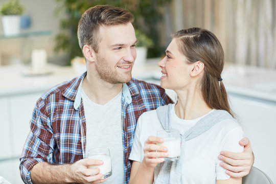 Yougn man and woman with glasses of milk looking at one another and talking by breakfast