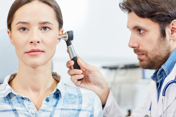 Young professional doctor examining ears of female patient in clinics