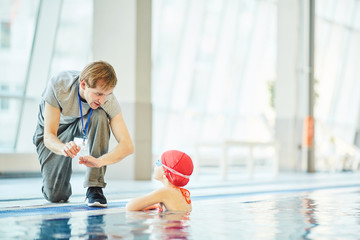 Young trainer explaining little swimmer what to do in extreme situation in water