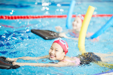 Cute girl having fun while learning to swim with special resistance inflatable equipment