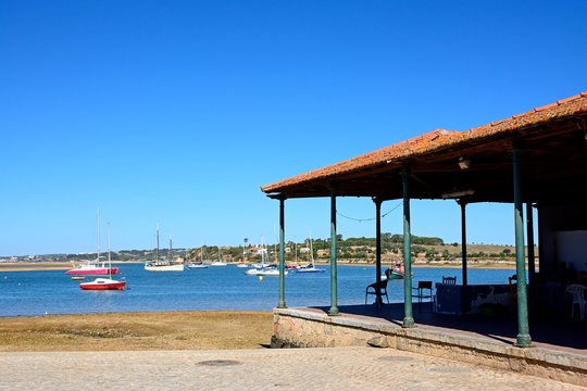 Yachts moored in the estuary with the fish market building to the right hand side in the foreground, Algarve, Portugal.