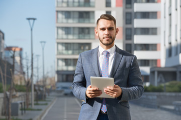 Businessman or real estate agent with tablet computer against new building
