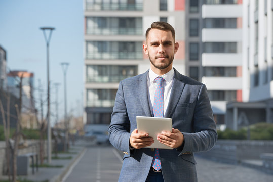 Businessman or real estate agent with tablet computer against new building