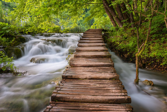 Beautiful view of waterfalls with turquoise water and wooden pathway through over water. Plitvice Lakes National Park, Croatia. Famous attraction, summer landscape.