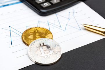 Two coins of bitcoin with calculator and pen on the graphs. Business and e-commerce concept.