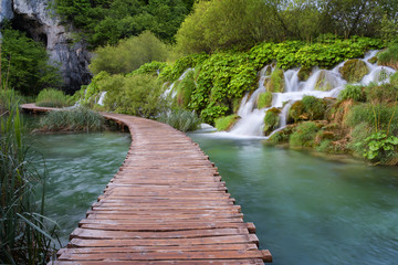 Beautiful view of waterfalls with turquoise water and wooden pathway through over water. Plitvice Lakes National Park, Croatia. Famous attraction, summer landscape.
