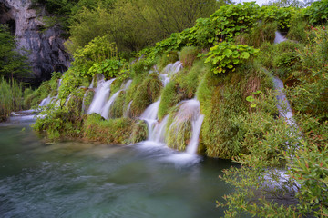 Beautiful view of waterfalls with turquoise water and wooden pathway through over water. Plitvice Lakes National Park, Croatia. Famous attraction, summer landscape.