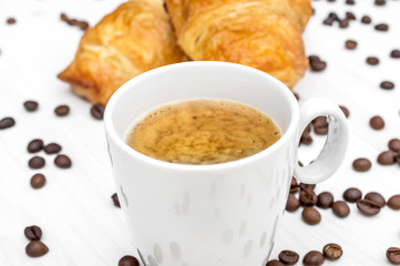 Cup of coffee, two croissants on napkin and coffee beans on the table. Close up.