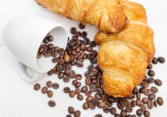 Coffee beans scattered from cup and two croissants on the table. Top view.