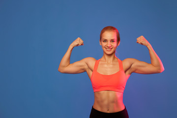 blond female athlete showing biceps on blue background,