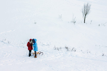 Fototapeta na wymiar two girls with sleds in an open area covered with snow, something is being considered