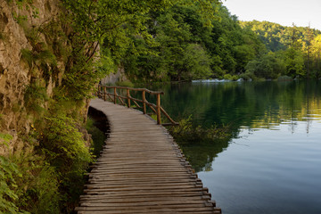 Fototapeta na wymiar Beautiful view of waterfalls with turquoise water and wooden pathway through over water. Plitvice Lakes National Park, Croatia. Famous attraction, summer landscape.