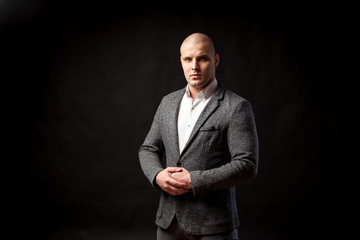 Young bald man in gray suit and white shirt posing on black isolated background