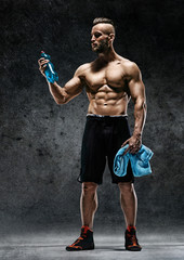 Fototapeta na wymiar Sporty man having a break. Photo of muscular man with water and towel in his hands on dark background. Health concept.