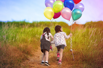 twin kids playing around on the meadow at the hills with holding in hand multicolor ballons