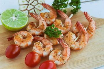 Skewers shrimp barbecue served on wood cutting board with lemon or lime and fresh cherry tomato. Delicious grilled prawn with spices for snacks in party. Homemade food concept of seafood menu.