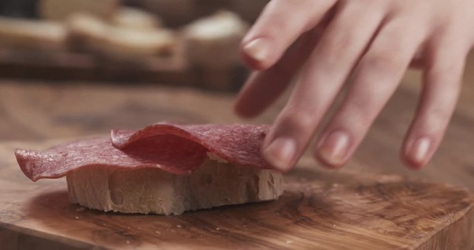 Slow motion young female hand take baguette slice with cream cheese and salami from wood board