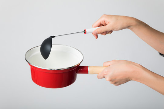 Hand holding a  single-handled pot and a ladle.